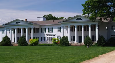 The historic white colonial-style Thompson Manor with large pillars and a manicured green lawn.